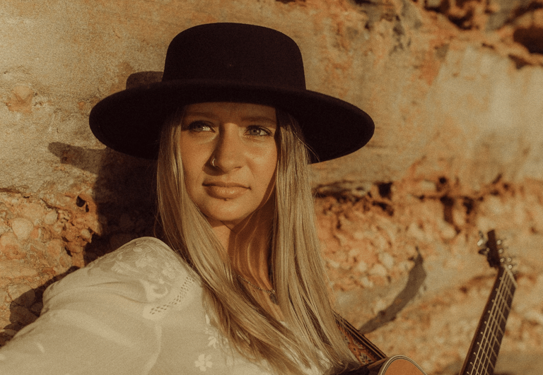 Person wearing a black wide-brimmed hat and white shirt against a weathered, rust-toned brick wall.