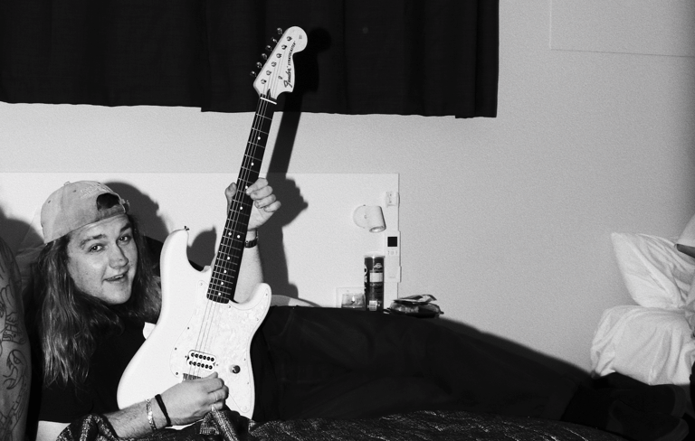 Musician with long hair holding a white electric guitar aloft in black and white photograph.