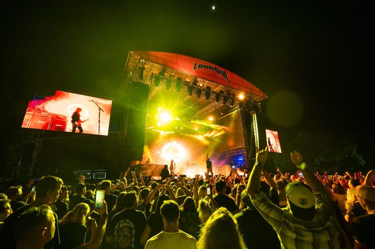 Large outdoor festival stage with bright yellow-green lighting surrounded by a dense crowd of attendees at night.