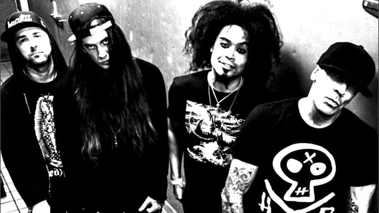 Four band members in dark clothing with long hair posed together in black and white photograph.