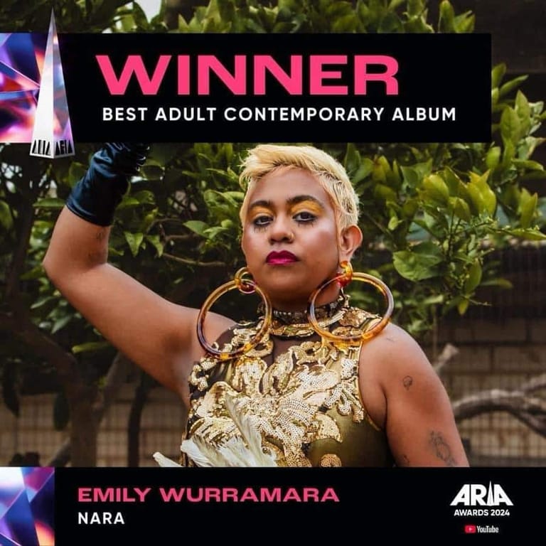 Emily Wurramara holds her fist aloft wearing gold jewellery against green foliage, with "Winner Best Adult Contemporary Album" text overlay.