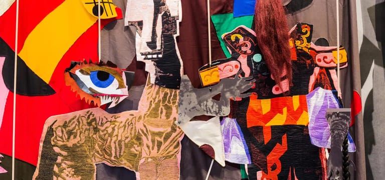 Colourful cardboard puppets and flags displayed against a red and yellow backdrop in an exhibition space.