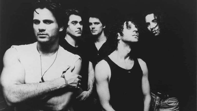 Five men posed against a dark background in a black and white band photograph.