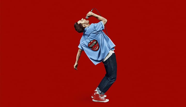 Person in blue shirt and dark pants jumping mid-air against a bright red background.