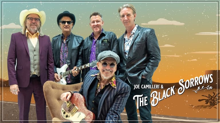 Joe Camilleri and The Black Sorrows band members posed together against a warm sunset background.