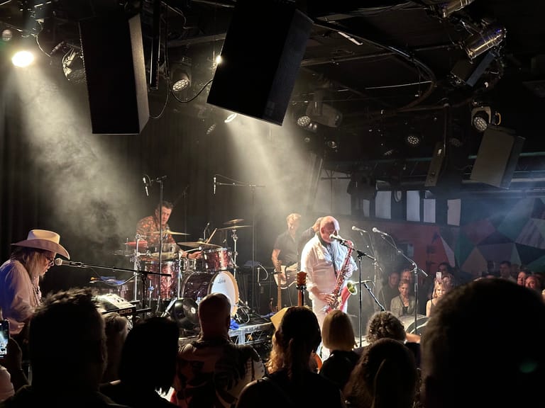 Live band performing on stage with dramatic lighting, audience silhouettes in foreground.