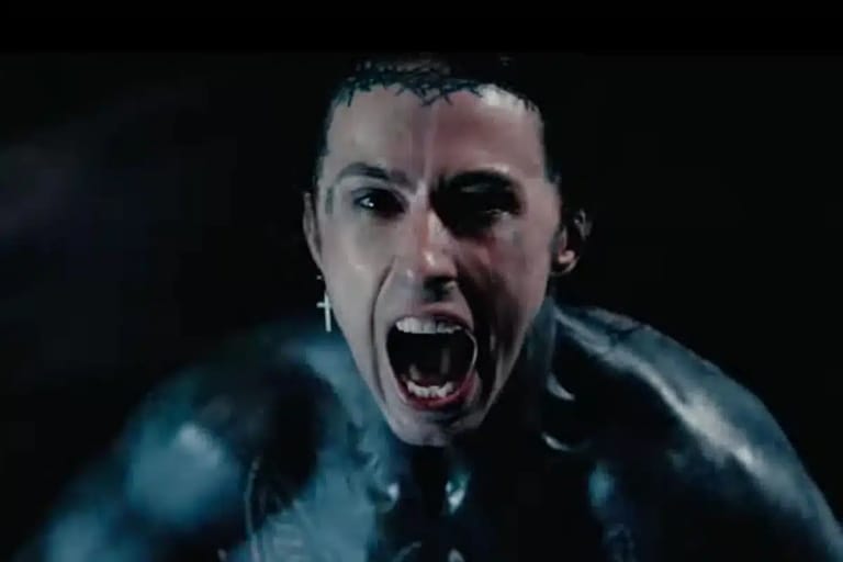 Man with dramatic facial expression and dark hair screaming intensely against a black background.