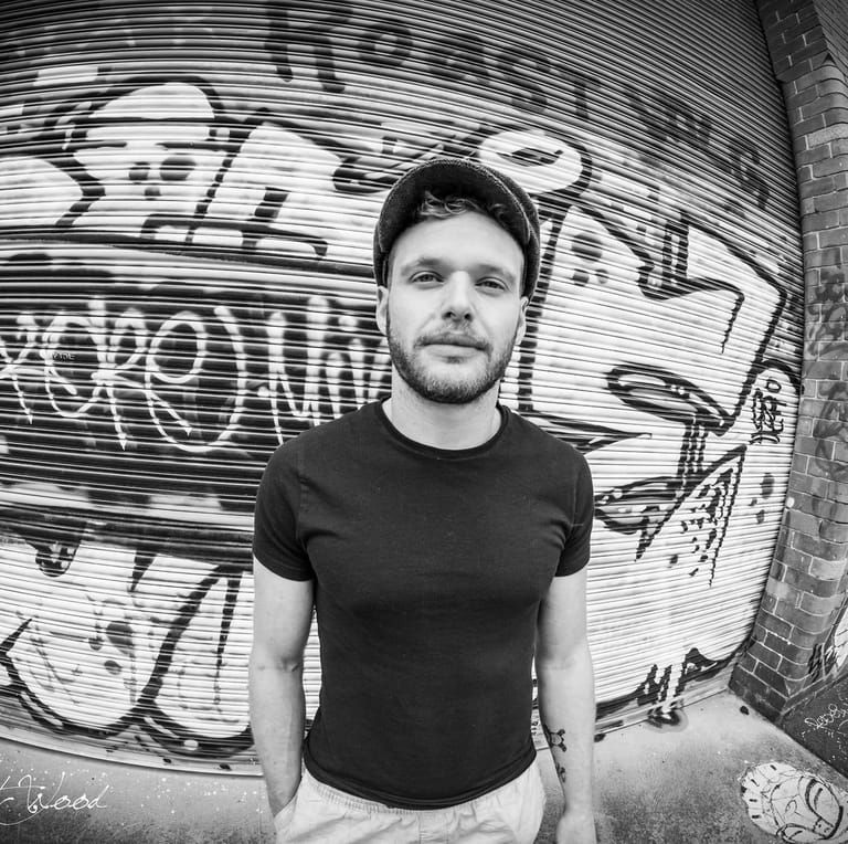 Man in black t-shirt posing against monochrome graffiti wall backdrop.