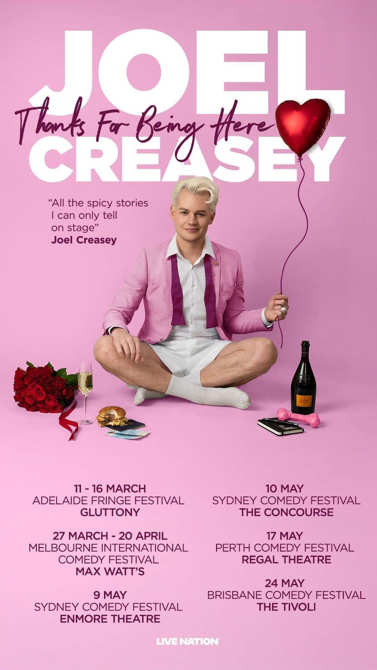 Man in pink jacket holding red heart balloon sits cross-legged against pink background for Joel Creasey comedy tour poster.