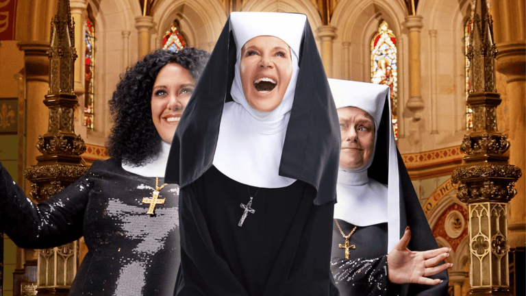 Three women in nun costumes perform in an ornate cathedral interior, centre figure with arms raised in theatrical celebration.