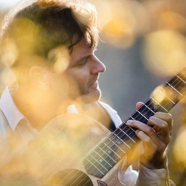Guitarist in profile playing classical guitar with warm, blurred bokeh lighting in the background.