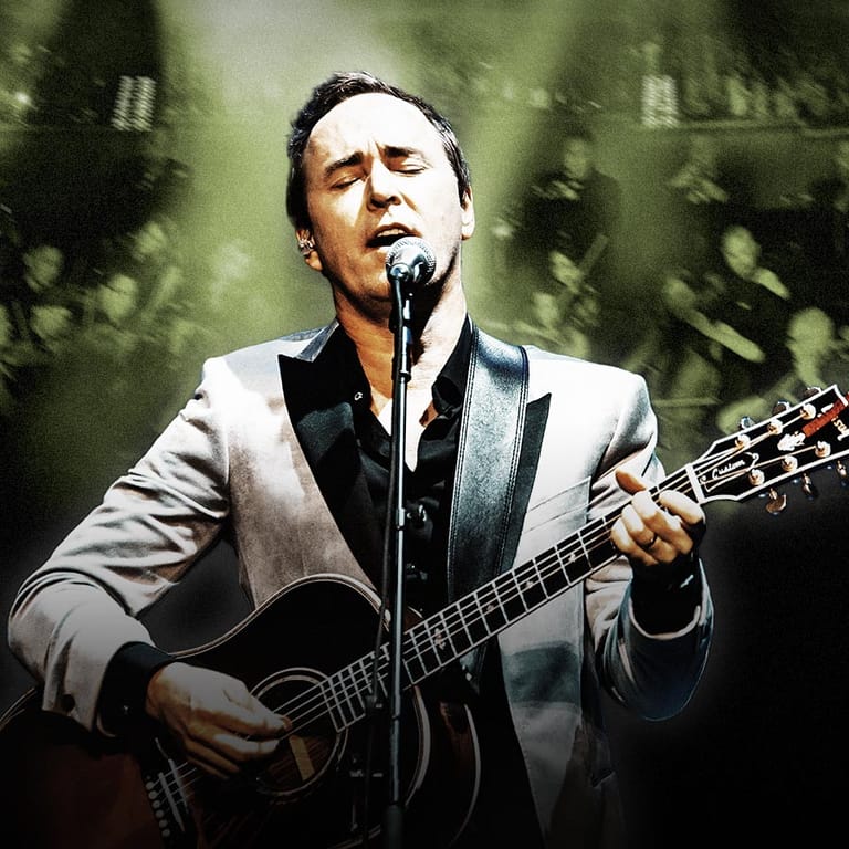 Male musician performing at microphone with acoustic guitar against muted green stage backdrop.