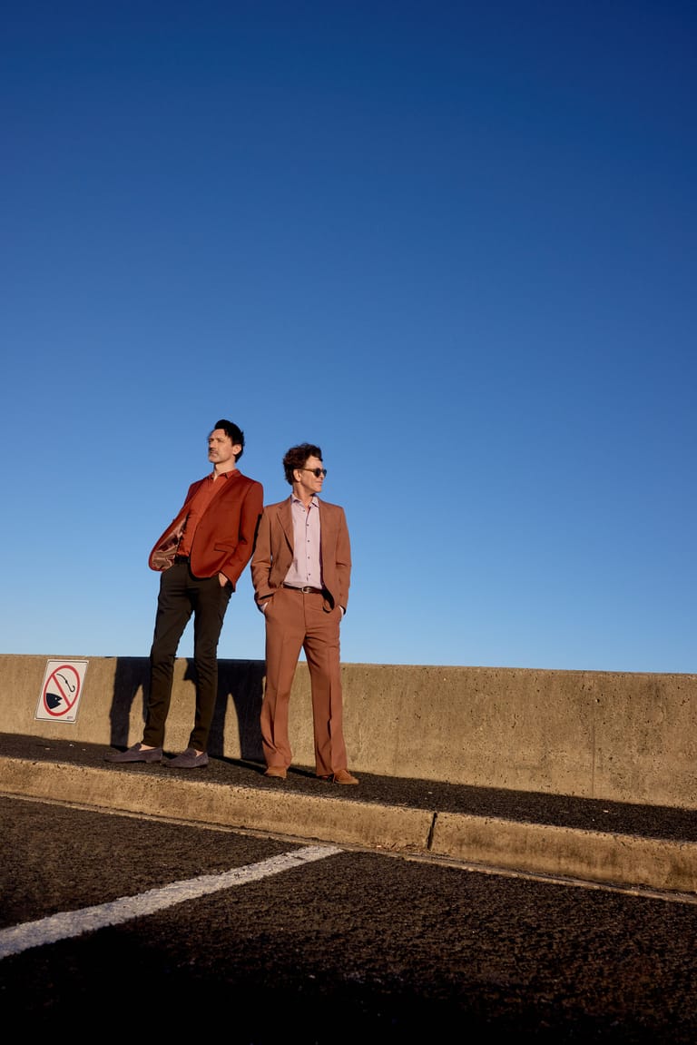 Two people in rust and tan suits stand on a concrete structure against a clear blue sky.