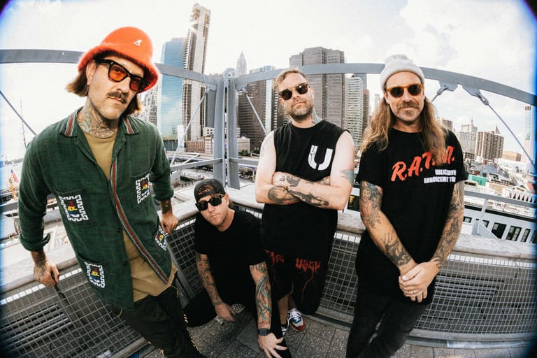 Four band members posed on a rooftop with a city skyline behind them.