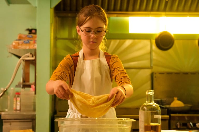Person in apron stretching golden dough over a bowl in a bright kitchen workspace.