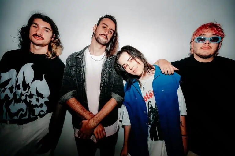 Four band members pose together against a white backdrop, smiling at the camera.