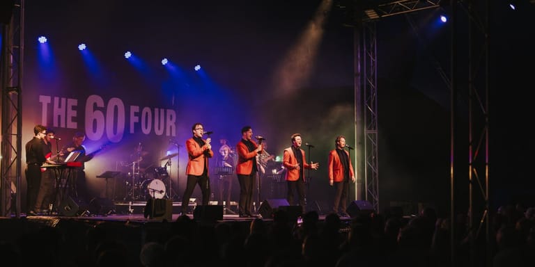 The Go-Go Four band performs on stage under blue and purple lighting with audience silhouettes in the foreground.