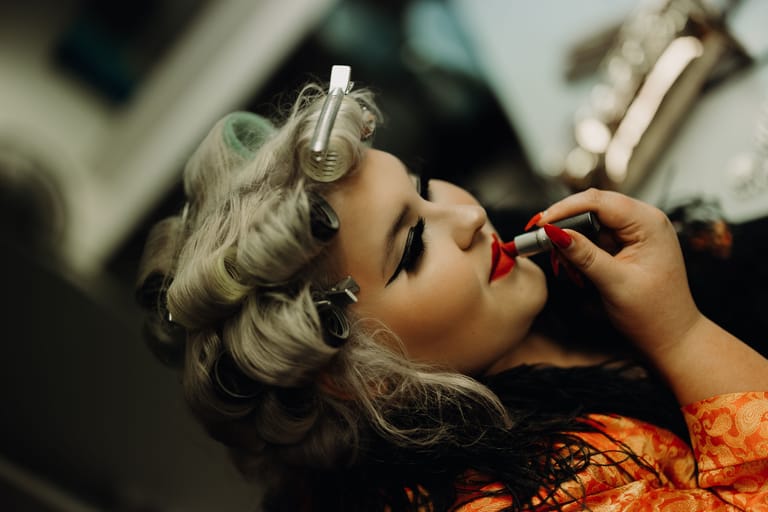 Makeup artist applies red lipstick to a model wearing vintage pin-up curls and styling.