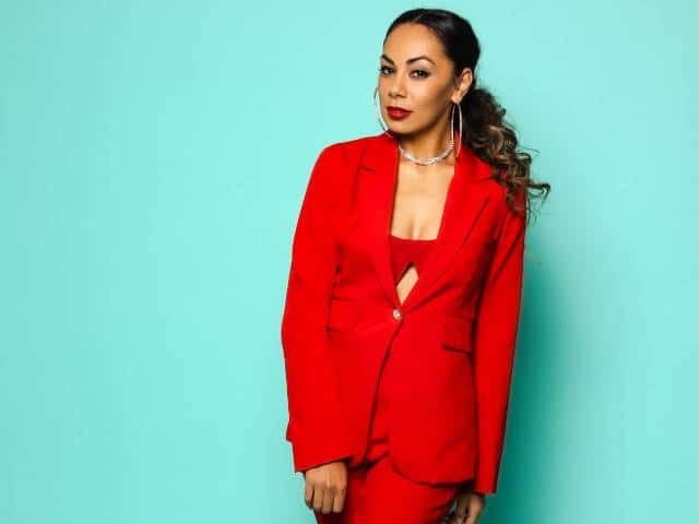 Woman in a red blazer and matching trousers against a turquoise background.
