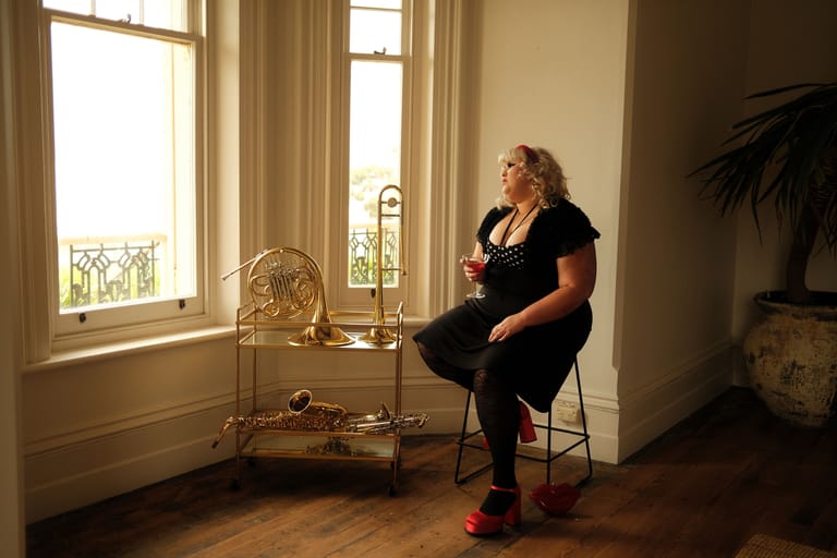 Woman in black clothing seated on a stool near tall windows during an interview setting.