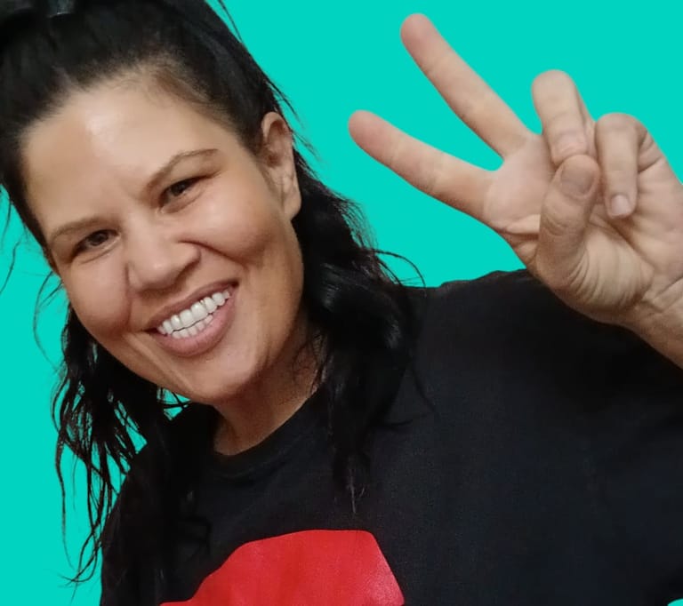 Woman in black shirt with red graphic smiling and gesturing against turquoise background.