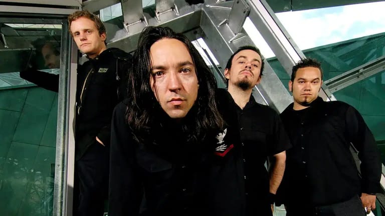 Four musicians in black clothing stand in a modern interior space with industrial green and grey tones.