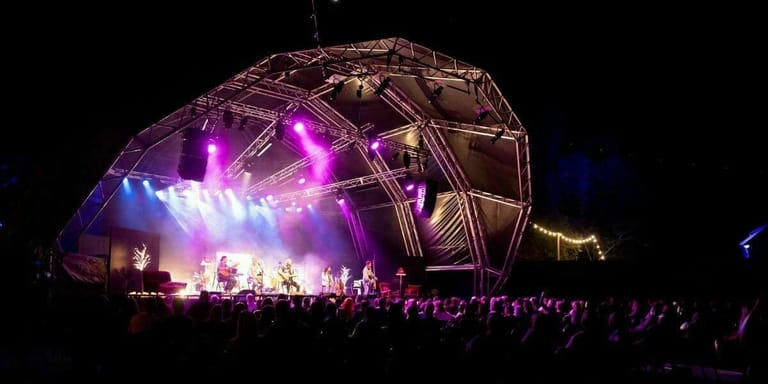 Large geodesic dome stage structure illuminated in purple and gold light, with performers and audience silhouettes visible at night.