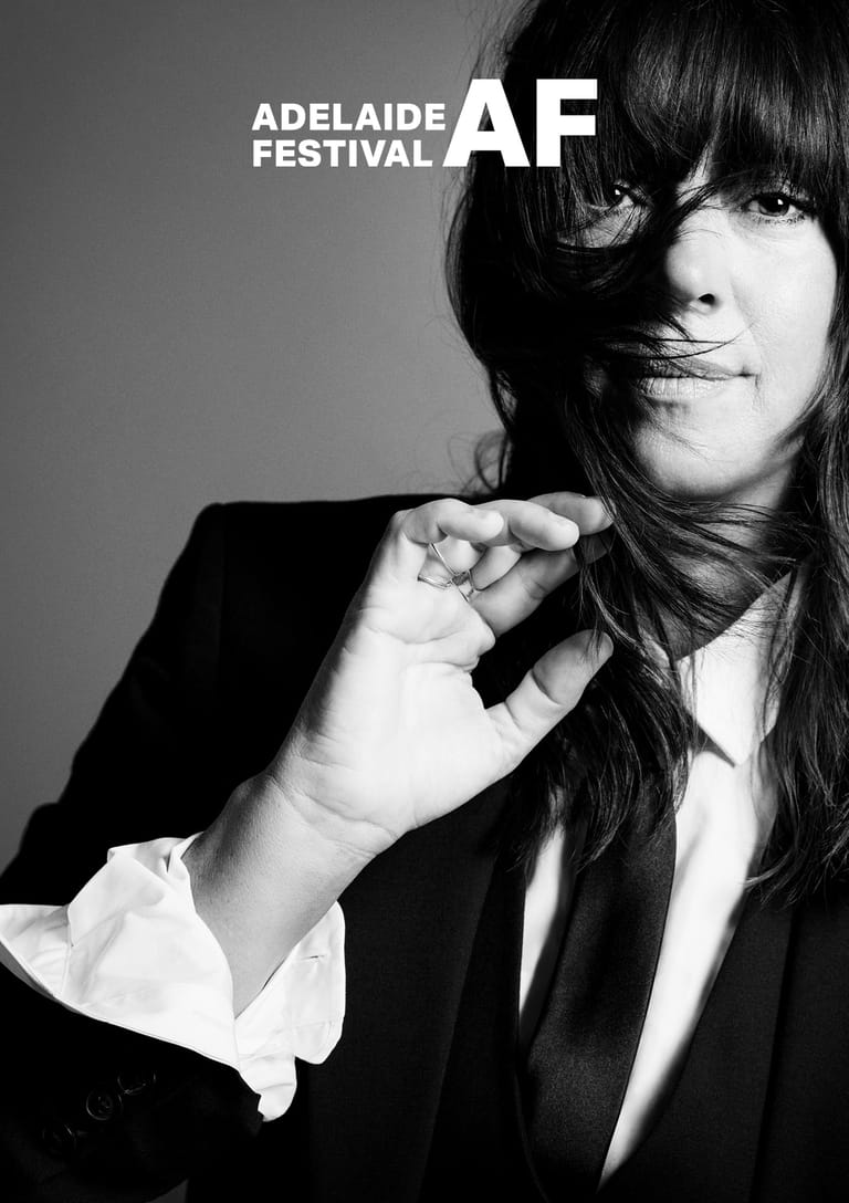 Person with dark hair and fringe in black blazer and white shirt against grey background for Adelaide Festival promotional image.