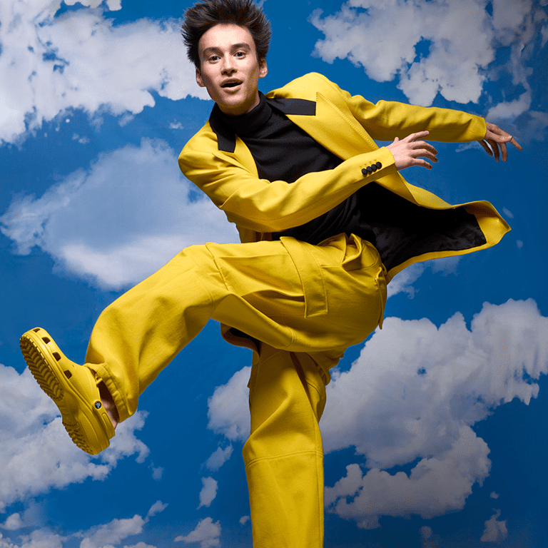 Person in bright yellow suit leaping dynamically against a blue sky with white clouds backdrop.
