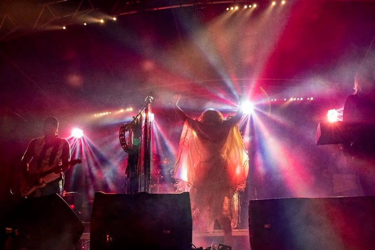 Performers on stage bathed in dramatic pink and purple stage lighting with atmospheric haze.