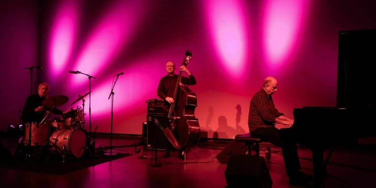 Jazz ensemble performing on stage bathed in vibrant magenta lighting and atmospheric silhouettes.
