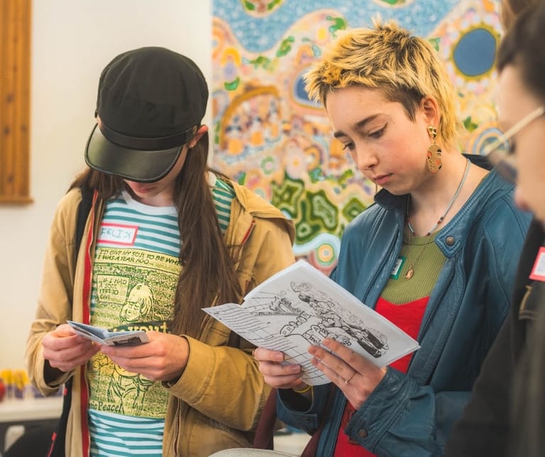 Two people examine a printed artwork together in a bright studio space decorated with colourful paintings.