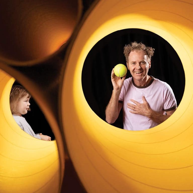 Man holding a green apple framed in a large yellow circular opening, with a child visible through a gap beside him.