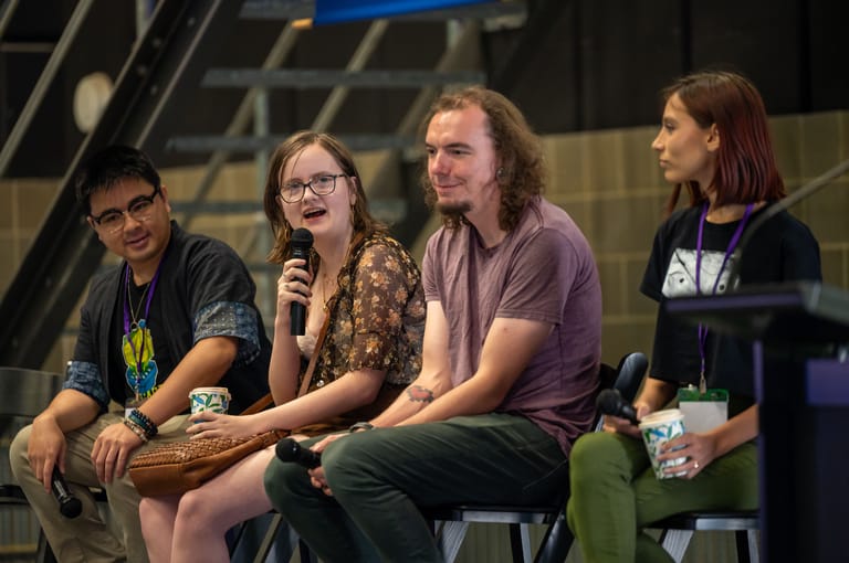 Four panellists seated on stage during a discussion, with one holding a microphone.