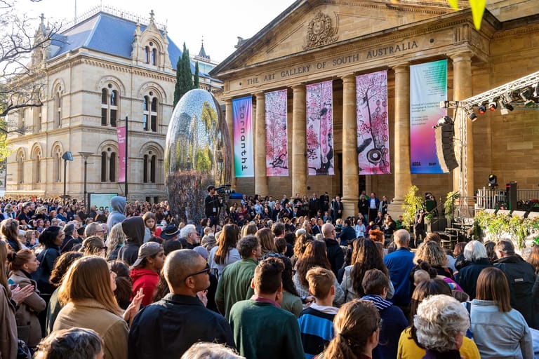 Large crowd gathered in a historic city square beneath ornate heritage buildings and colourful banners.