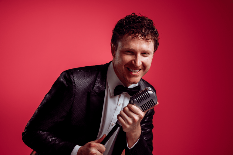 Man in black blazer and white shirt holding vintage microphone against red background.