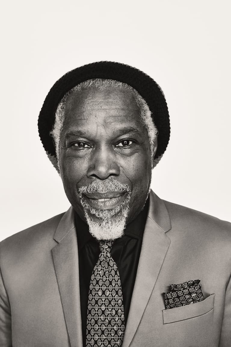 Man in grey suit and black beanie, with grey beard, photographed against a neutral background.