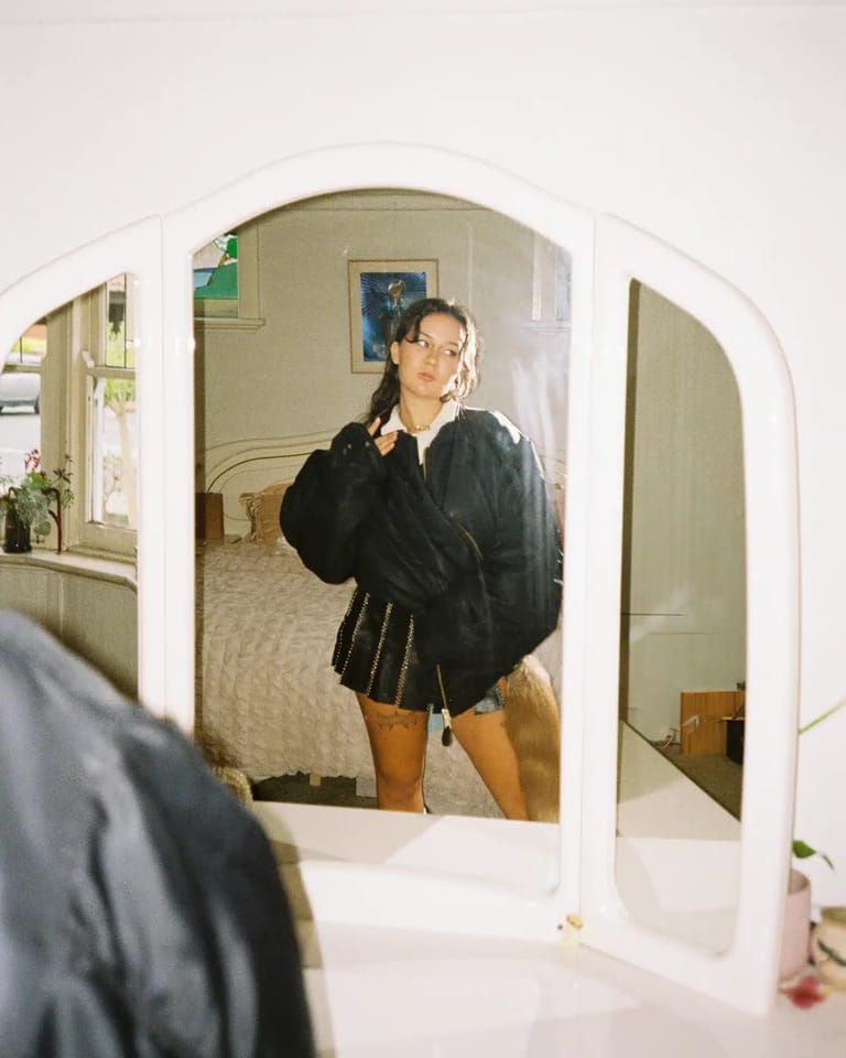 Person in black jacket adjusting glasses in bathroom mirror with white curved frame.