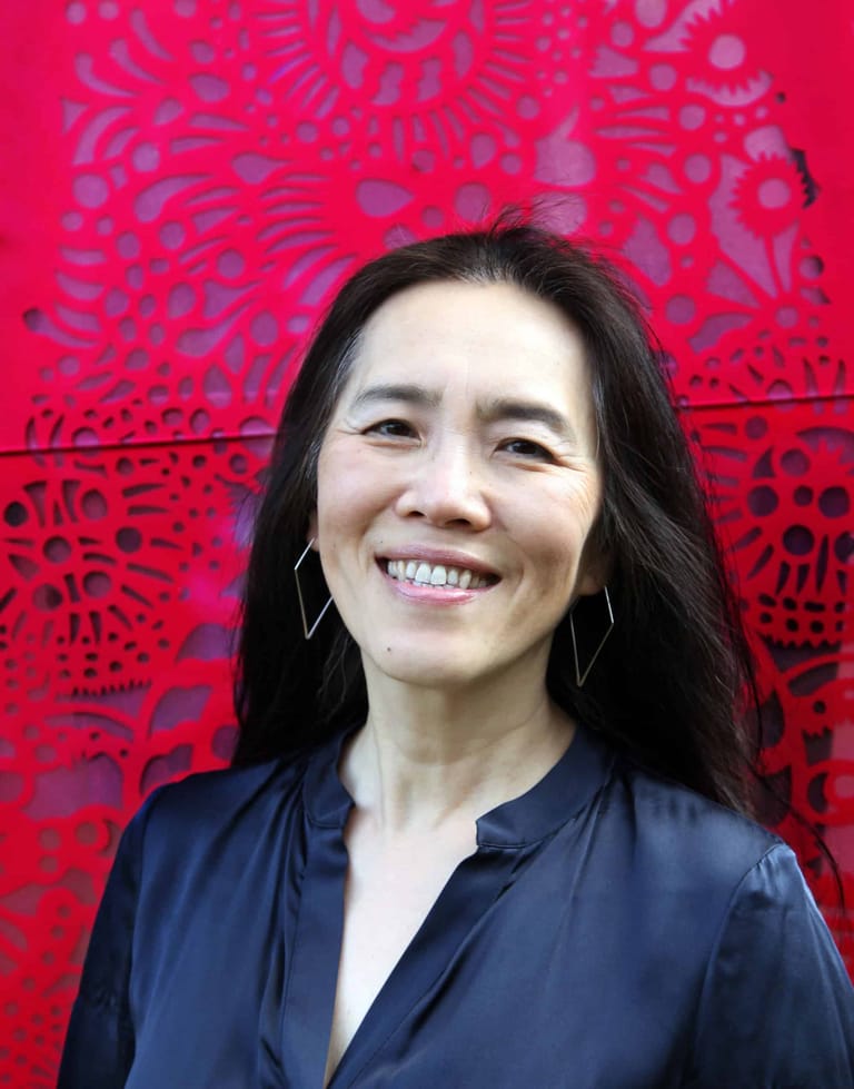 Woman with long dark hair smiling at camera against vibrant red patterned backdrop.