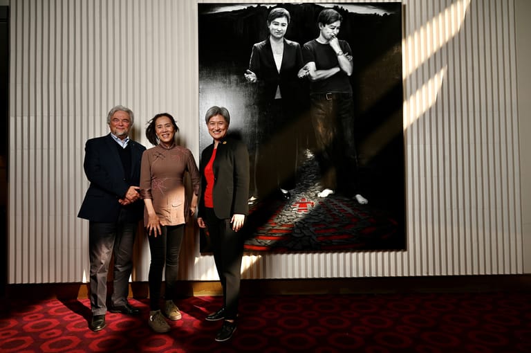 Three people stand before a large black-and-white film still in a gallery space, red carpet beneath their feet.