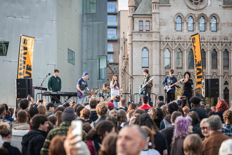 Outdoor stage performance in front of historic cathedral with crowd gathered in urban plaza.