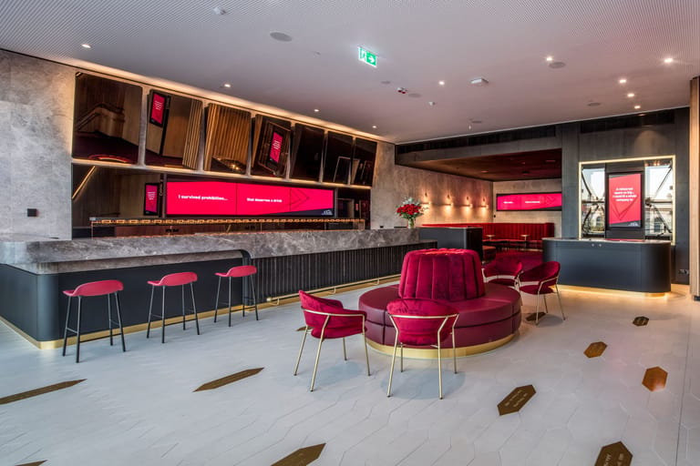 Modern bar lounge with neon pink signage, burgundy seating, and minimalist décor in a contemporary venue.