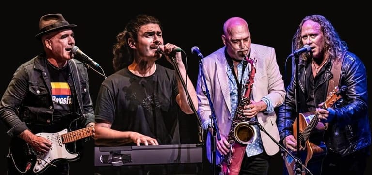 Four musicians performing on stage with guitar, vocals, saxophone and keyboard under coloured stage lighting.