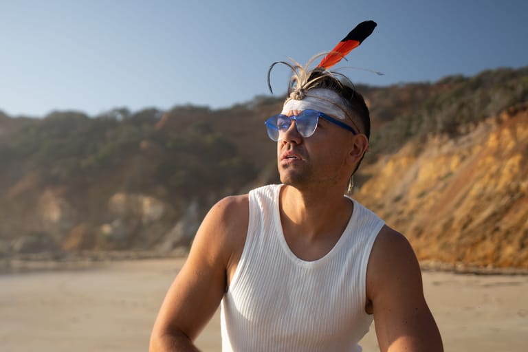 Man wearing snorkel gear and sunglasses on a beach with cliffs in the background.