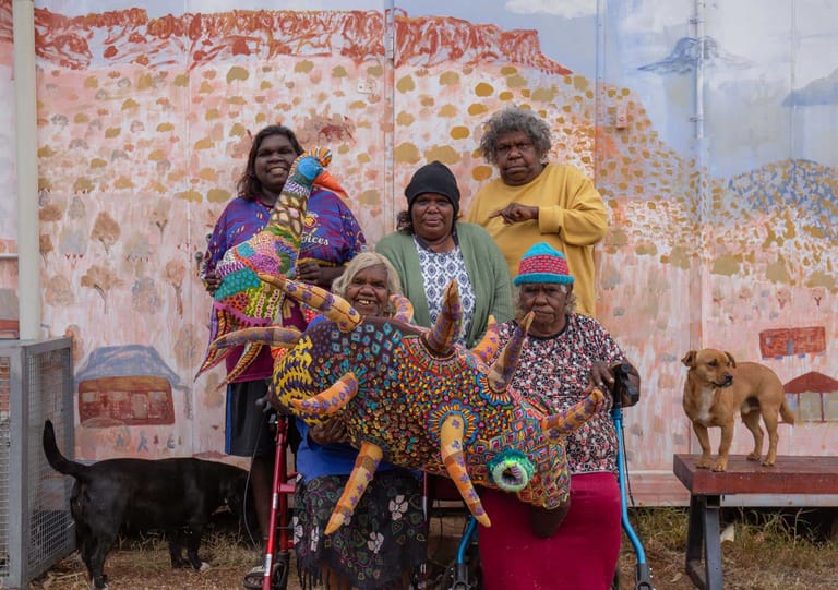 Group of people in colourful clothing posing with dogs in front of a large patterned fabric backdrop.