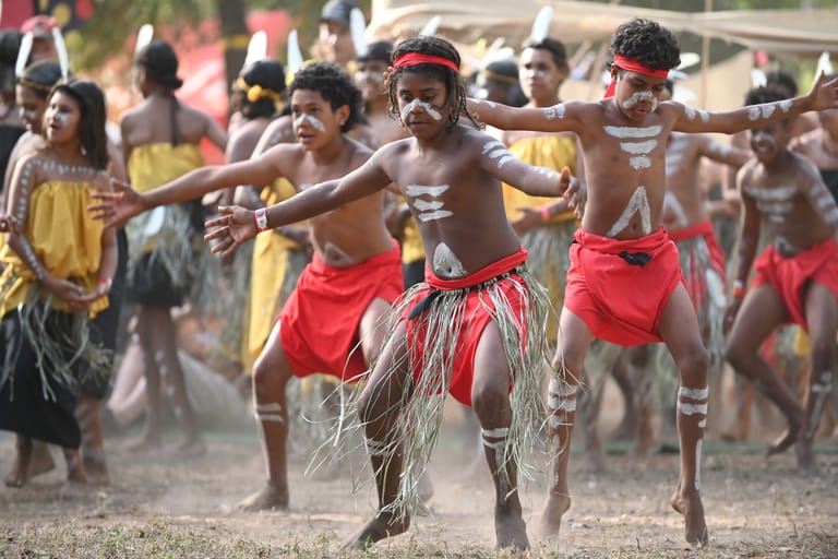 Group of Indigenous performers in traditional grass skirts and body paint dancing together during a cultural celebration or festival.