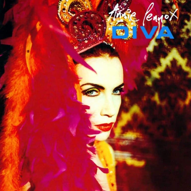Person wearing elaborate red and gold feathered headdress against vibrant pink and yellow lighting.