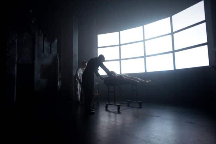 Silhouetted figure seated against a large gridded window casting bright light across an empty studio space.