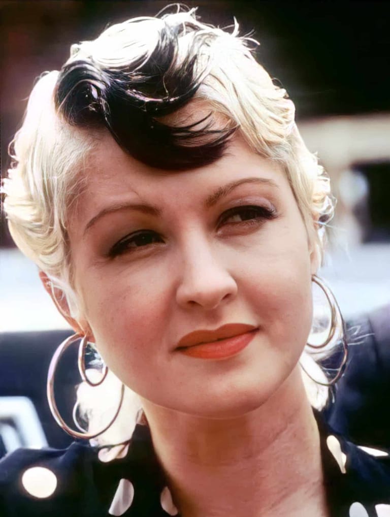 Person with two-tone blonde and black styled hair wearing hoop earrings and orange lipstick.