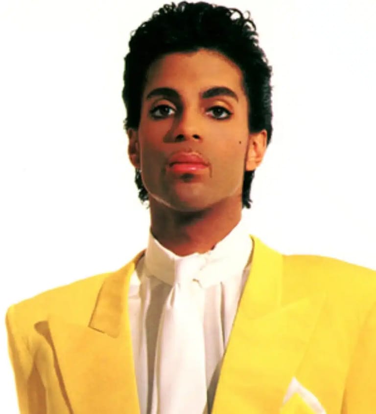 Portrait of a performer in a bright yellow blazer and white shirt against a plain background.